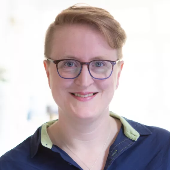 A photograph of Ruth Cheesley wearing glasses and a dark blue collared shirt with a contrasting green trim on the collar.